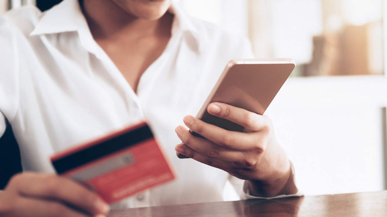 a woman holding a card and a mobile phone; image used for HSBC Sri Lanka credit card useful links page.